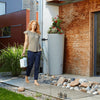Image of Woman walking on a wooden deck with a water container, next to a Natura 2in1 MiniTank cylindrical concrete tank