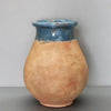 Image of A handmade ceramic vase with a rounded, bulbous body in a warm, textured terracotta orange-brown glaze, and a contrasting blue glazed neck with small orange floral details, set against a neutral gray background.