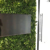 Image of Green Tropics Artificial Plant Wall Panel installed on a wall with a mounted television, positioned beside a glass door