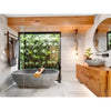 Image of Green Tropics Artificial Plant Wall Panel installed outside the bathroom’s glass window featuring a bathtub, towel rack, wooden sink with basin, and a mirror above