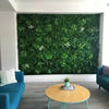 Image of Green Tropics Artificial Plant Wall Panel installed indoors on a clean white concrete wall complemented by a modern table and cozy couches