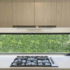 Image of Green Tropics Artificial Plant Wall Panel installed outdoors as a backdrop, overlooking the kitchen glass window with stove and cabinets inside