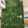 Image of Green Tropics Artificial Plant Wall Panel mounted on a large indoor feature wall in a modern office complemented by ceiling lights and nearby workstations