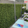 Image of Close up view of the Artificial Premium Natural Buxus Panel installed on a fence, surrounded by various pots containing artificial plants