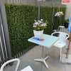 Image of Artificial Premium Natural Buxus Panel installed on a fence outdoor with seats, table and pots with artificial plants