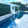 Image of Artificial White Tropics Vertical Garden Wall Panels paired with an artificial wall disc installed along the length of a white boundary wall in a modern backyard pool area