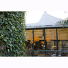 Image of Outdoor seating area with people dining under a white tent, surrounded by vertical greenery.