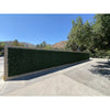 Image of Artificial Boxwood Hedge Plant Wall Screening Panels and a light tan frame stands in a paved outdoor area, contrasting with rolling hills and trees