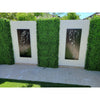 Image of A modern decorative wall with alternating Artificial Deluxe Buxus Hedge Wall Panels and black laser-cut metal panels featuring nature motifs, above light paved stones and a corner of turf