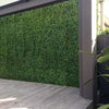 Image of An outdoor deck featuring a vibrant Artificial Jasmine Hedge Plant Wall Screen framed by dark gray architecture and weathered gray diagonal wooden decking