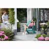 Image of Two people sitting on a porch with teal Adirondack chairs, surrounded by flowers and plants.
