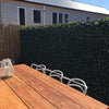 Image of Artificial Jasmine Hedge Extendable Trellis Screen installed on a patio fence with a wooden table in the foregound