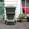 Image of Green hungry bin on wheels outside a house with plants around

