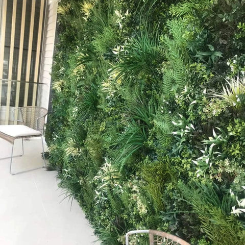 Artificial Green Forest Vertical Garden Panel installed on a wall in a patio area with white paving and a eat in front of the wall
