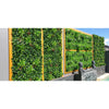 Image of Artificial Green Meadows 1m x 1m Plant Wall Panel UV Stabilised installed on a concrete wall with wooden accents styled with figurines and displayed beside a swimming pool