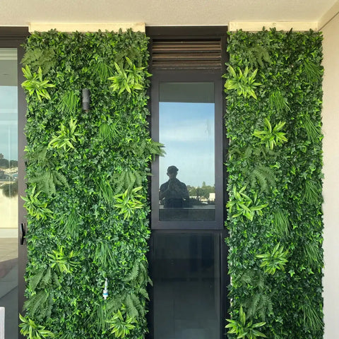 Green Tropics Artificial Plant Wall Panel installed outdoors on both sides of a tall glass window and door 