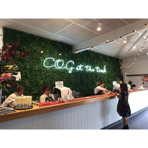 Green Tropics Artificial Plant Wall Panel installed with LED letter lighting on the wall behind the counter as a backdrop for staff in a coffee shop