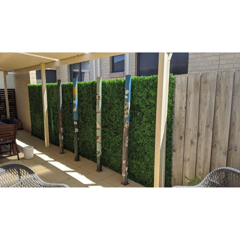 Artificial Mixed Boxwood 1m x 1m Plant Panel UV Stabilised mounted along a patio fence set against brick and timber with decorative painted poles in front
