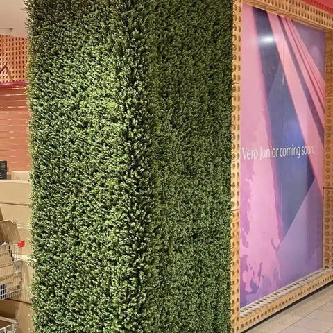 Artificial Premium Natural Buxus Panel mounted on a surrounding wall inside a mall, positioned next to a poster