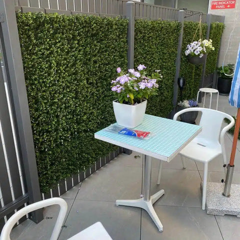 Artificial Premium Natural Buxus Panel installed on a fence outdoor with seats, table and pots with artificial plants