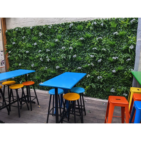 Artificial White Tropics Vertical Garden Wall Panels installed on a concrete wall in an outdoor setting with tables and chairs