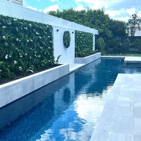 Artificial White Tropics Vertical Garden Wall Panels paired with an artificial wall disc installed along the length of a white boundary wall in a modern backyard pool area