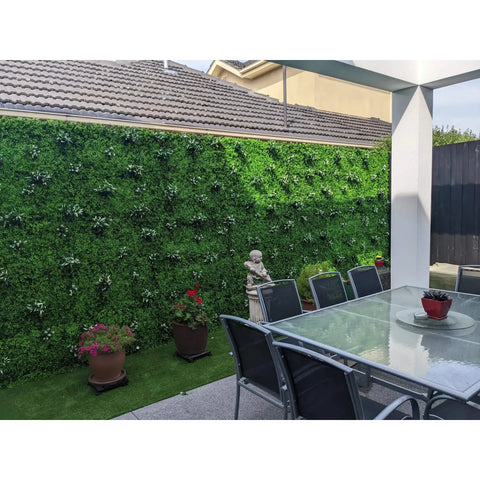 A covered outdoor patio featuring floor to ceiling Artificial Deluxe Buxus Hedge Wall panels, a glass dining table, chairs and a turf strip with plants and a decorative statue