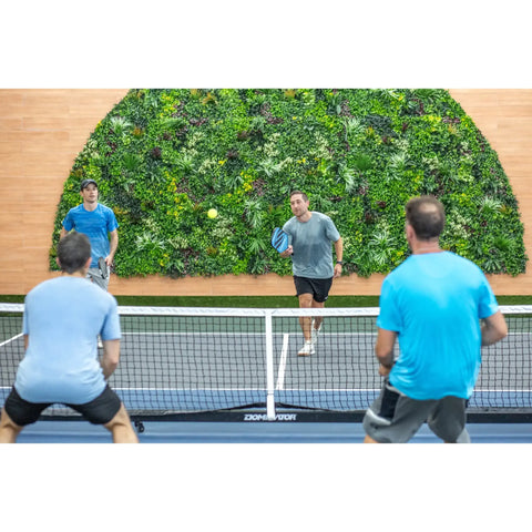Evergreen Rainforest Recycled Artificial Green Wall Panel framed by wood toned wall paneling with four men actively playing a doubles match of pickleball
