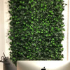 Image of An image of a workspace featuring the Artificial Ivy Leaf Hedge Panel as a green backdrop behind a desk with a silver Apple monitor and minimalist dark gray lamp