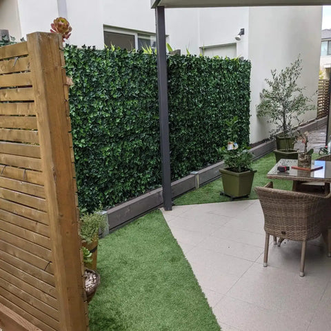 Modern patio with a wooden privacy screen and Artificial Ivy Leaf Hedge Panels featuring a tiled seating area and a strip of vibrant artificial grass