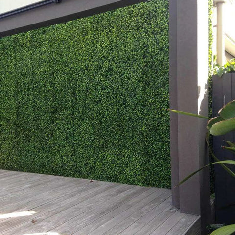 An outdoor deck featuring a vibrant Artificial Jasmine Hedge Plant Wall Screen framed by dark gray architecture and weathered gray diagonal wooden decking