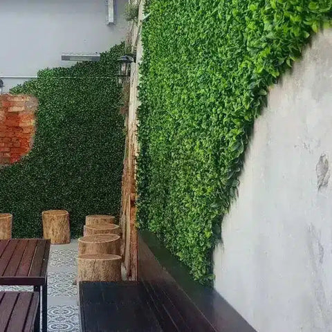 A stylish outdoor patio with Artificial Jasmine Hedge Plant Wall Screen Panels, an exposed red brick accent, rustic wooden seating, and patterned gray and white tile flooring