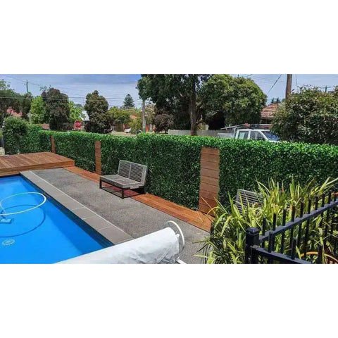 A modern backyard pool area with a privacy fence of Artificial Jasmine Hedge Plant Wall Screen Panels and timber posts, a wooden deck with bench, textured poolside path, and safety fence