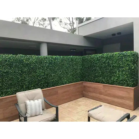 A contemporary patio with tall Artificial Jasmine Hedge Plant Wall Screen Panels in a wood look planter, light-tiled floor, and modern seating against a minimalist gray building