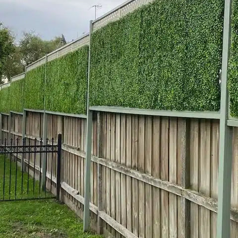 A long wooden fence upgraded with a gray frame, Artificial Jasmine Hedge Plant Wall Screen Panels, and matching lattice in a residential backyard with a small black gate