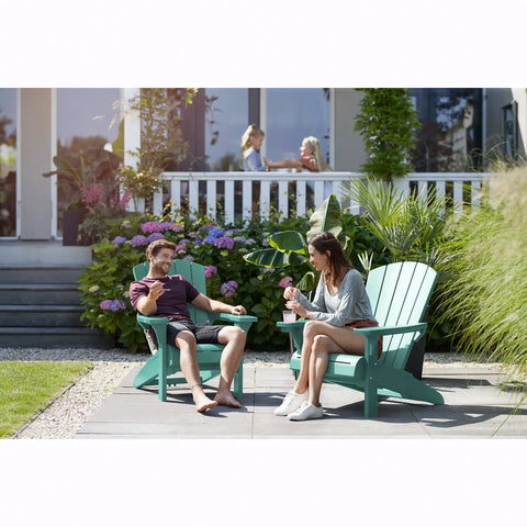 Two people sitting on teal Adirondack chairs in a garden setting.