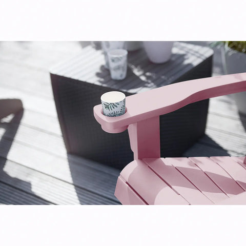 Pink adirondack chair with a cup holder containing a white cup with green pattern on a wooden deck.