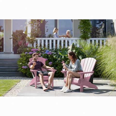 Two people sitting on pink Adirondack chairs in a garden setting.