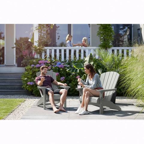 Two people sitting on Adirondack chairs in a garden setting.