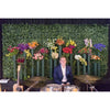Image of A young man smiles behind a drum set in front of dense Artificial Laurel Hedge Plant Wall Screening Panels adorned with colorful flower bouquets, with an acoustic guitar and a drum set nearby