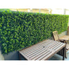 Image of An outdoor patio with Artificial Spring Sensation Hedge Wall Panels installed as the backdrop to a wooden table and chair in the seating area