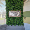 Image of A building exterior with Artificial Spring Sensation Hedge Wall Panels as a backdrop for a vintage-style "Yates Seeds" sign with a colorful side stripes and the number "37"