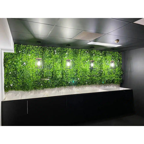 Artificial White Oasis Vertical Garden Panel installed to a wall accented by four warm lantern style lights. Below is a black cabinet with a white countertop all framed by a modern ceiling with lighting and ventilation