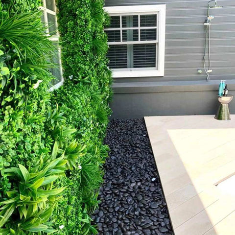 Artificial White Oasis Vertical Garden Panel installed on a wall between two windows along the black stone pebbled walkway