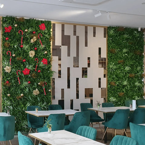 Wild Tropics Artificial Vertical Garden Panels installed indoors, with one decorated for Christmas and the other plain, beside white marble tables and teal chairs separated by a geometric partition wall